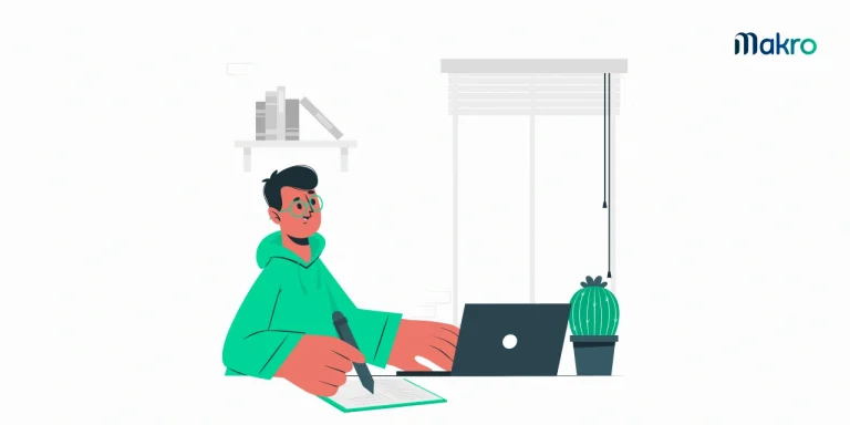 Um homem com roupas de frio opera um computador enquanto escreve em um caderno simultaneamente. Ao lado do computador, há um cacto.