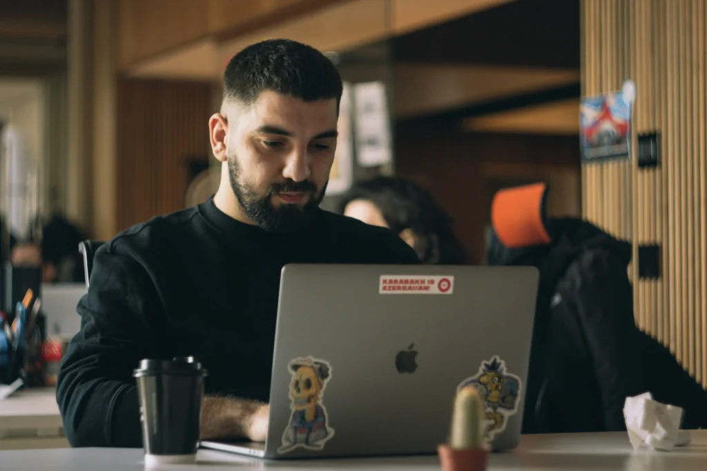 Homem sentado em um coworking em frente a tela de um computador acessa um sistema contábil ou software para contadores grátis para pequenas empresas