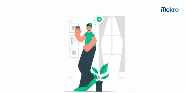 Um homem com touca na cabeça mexendo em seu celular enquanto está encostado em um vaso de planta com uma planta dentro.