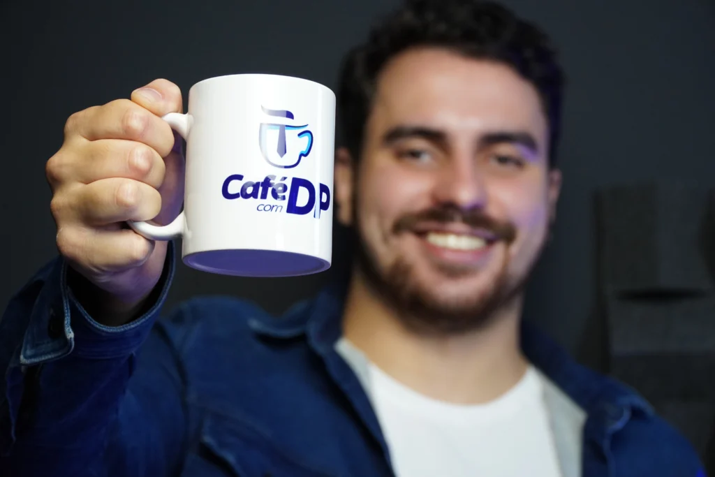 Thales, colaborador da Makro, sorrindo e mostrando uma caneca do Café com Dp, um quadro do YouTube da Makro.