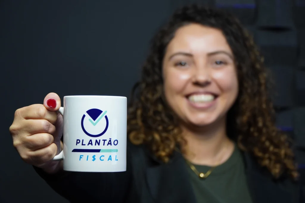 Vanessa, colaboradora da Makro, sorrindo e mostrando uma caneca do Plantão Fiscal, um "quadro" do YouTube da Makro.