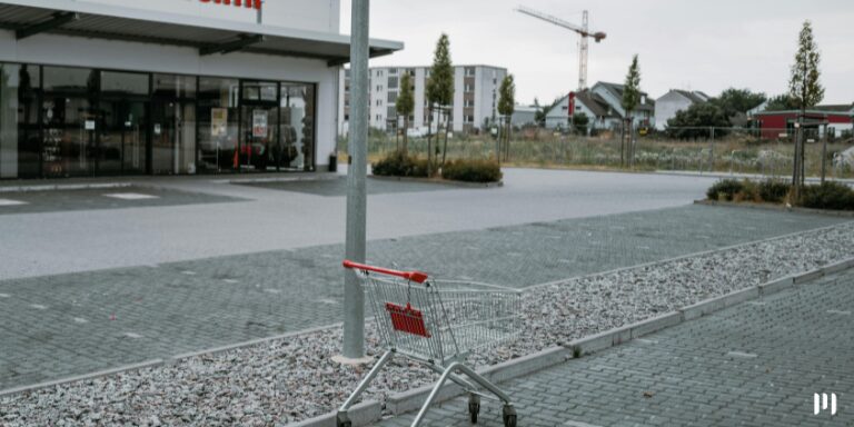 A imagem mostra um carrinho vermelho abandonado em uma loja de conveniência, aparentemente fechada. A ideia é fazer uma alusão ao cado da Fraude na Americanas