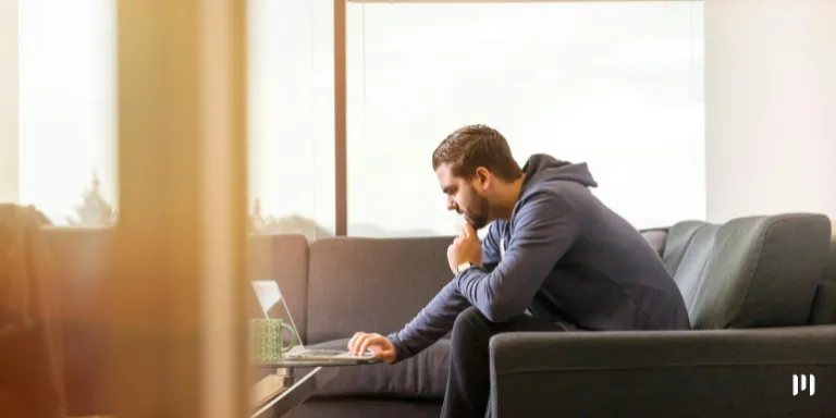 Homem sentado no sofá olha para a tela do computador onde está vendo a notícia sobre como ficará o Simples na Reforma Tributária