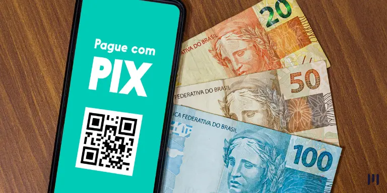 Um celular com a tela exibindo 'Pague com o PIX' e um QR Code abaixo. Ao lado, notas de dinheiro. A imagem ilustra o Pix Agendado Recorrente.