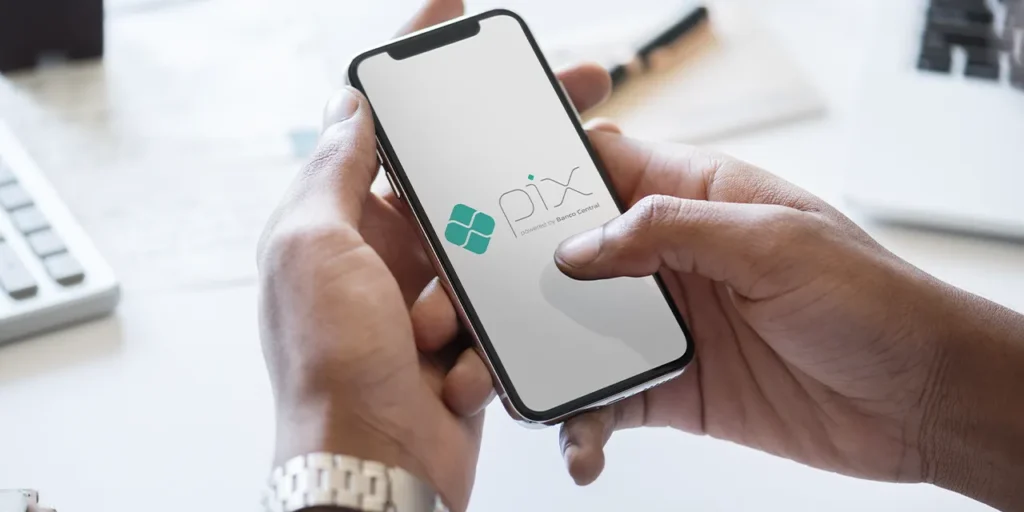 Imagem de uma pessoa segurando um celular com a logo do pix centralizado no meio da tela do celular.