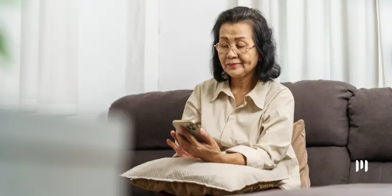 Idosa consulta informações sobre o segundo lote de restituição do IRPF pelo celular em sua residência.